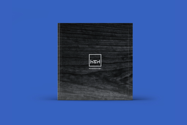 A sleek black journal with an embossed Hugo & Hoby geometric logo centered on a textured cover, against a vibrant blue background.
