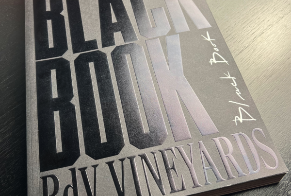 A sleek black book with embossed lettering that reads "Black Book No. 1 RDV Vineyards" placed on a dark wooden surface, hinting at a luxurious wine experience.