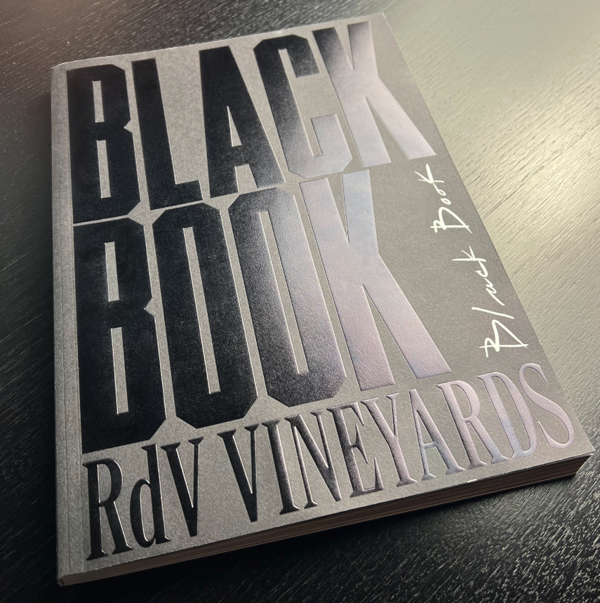 A sleek black book with embossed lettering that reads "Black Book No. 1 RDV Vineyards" placed on a dark wooden surface, hinting at a luxurious wine experience.