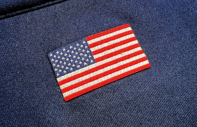 An embroidered u.s. flag patch attached to a dark blue denim fabric, with detailed stitching visible on the flag and denim texture.
