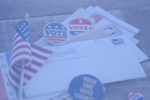 A collection of Political Campaign Print materials, including envelopes, "I Voted" stickers, a small American flag, and buttons with voting messages, are displayed on a wooden surface. The overall image has a blue tint.