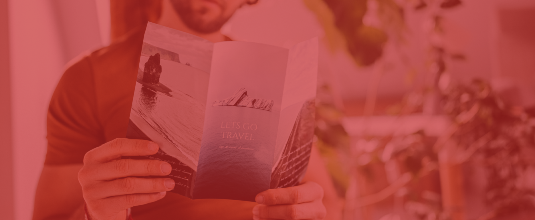 A person holds a travel brochure titled "Let's Go Travel," capturing a scenic ocean view, perfect for the holiday season. The image has a red overlay, with blurred plants in the background, setting an engaging tone for personalized print campaigns.