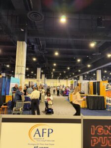 A busy convention hall buzzes with marketing teams and attendees discussing fundraising among exhibition booths. The AFP (Association of Fundraising Professionals) Washington DC Metro Area Chapter sign stands out in the foreground at the BRIDGE Conference.